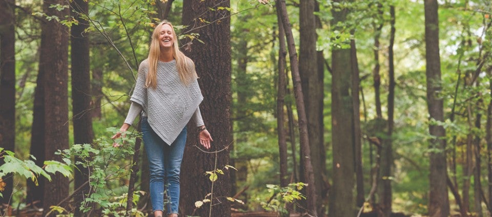 Find Your Escape Smiling woman with arms lowered and eyes closed standing in the woods.